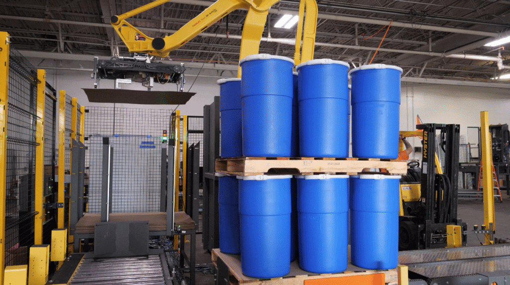 Robotic palletizer lifting blue drums from a pallet in an industrial setting, highlighting PASCO® Systems' automated drum palletizing capabilities.