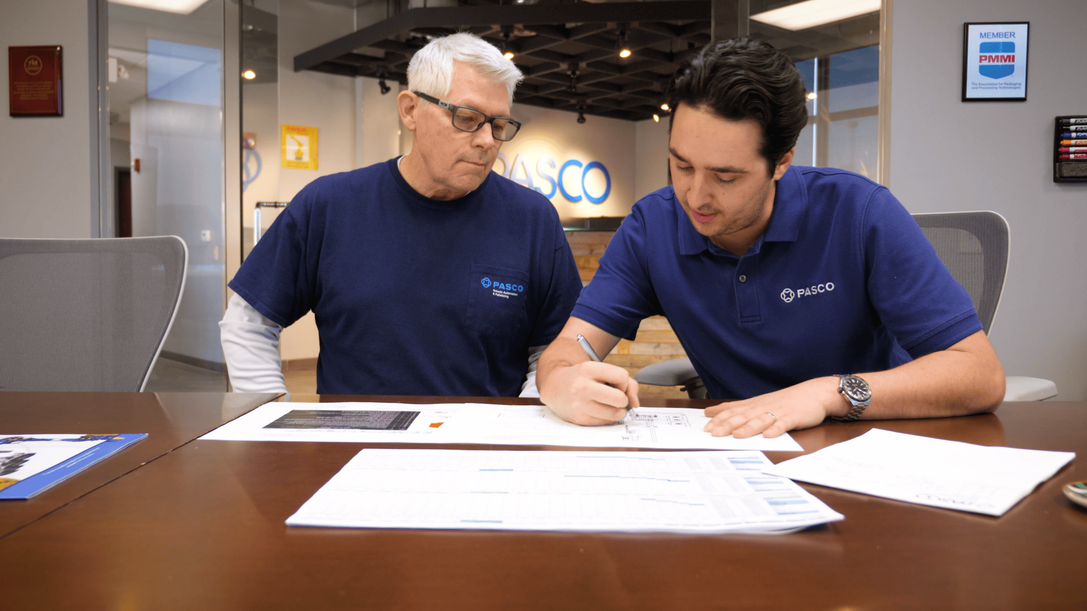 Two PASCO Systems employees collaborating at a table, reviewing engineering documents and design plans, showcasing teamwork and innovation in automation solutions.